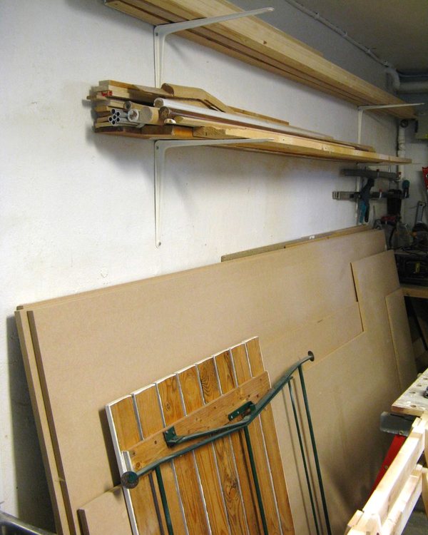 Sheet material stacked against the wall under wall-mounted brackets holding mouldings