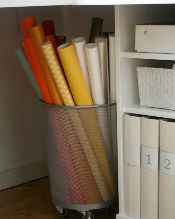 The bin of wrapping paper rolls on its castors beside a white cupboard