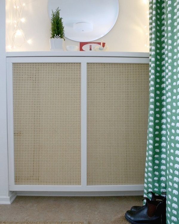 The caned radiator cover under a round mirror beside a green curtain